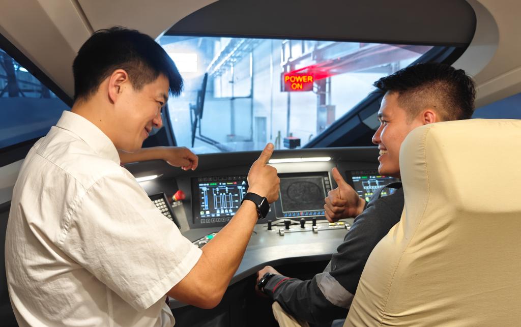 8月25日，在印度尼西亞萬隆的雅萬高鐵德卡魯爾動車所內(nèi)，中國師傅穆振（左）在向印尼火車司機塞蒂亞萬講解動車組出庫前的上電作業(yè)。