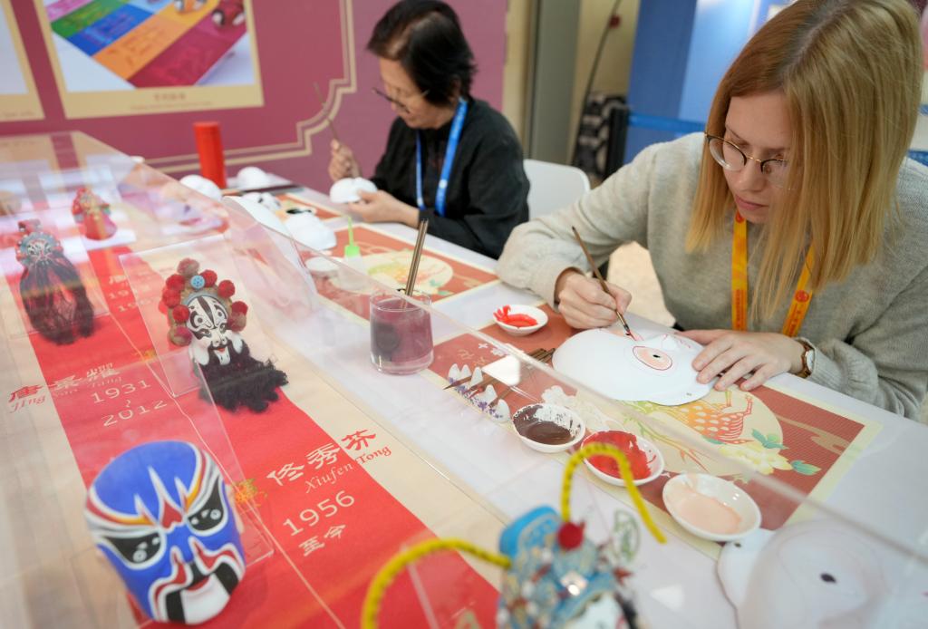 10月16日，在第三屆“一帶一路”國際合作高峰論壇新聞中心，來自比利時(shí)的記者（右）體驗(yàn)畫京劇臉譜。新華社記者 王毓國 攝