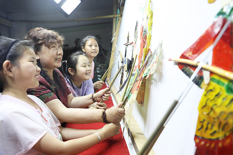 皮影藝人指導(dǎo)小朋友表演皮影戲。