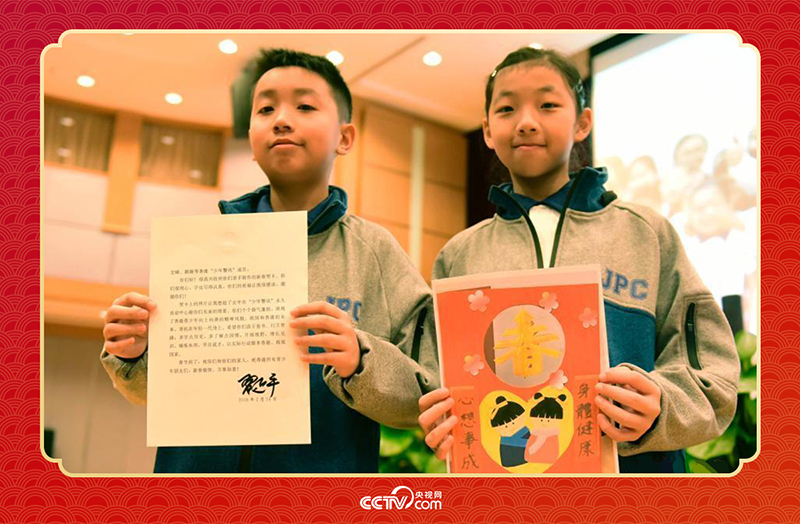 圖為香港“少年警訊”成員郭宏晞（左）展示習(xí)主席回信、羅顥凝（右）展示送給習(xí)主席的賀卡并合影。