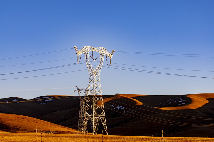 阿里地區(qū)的曠野上，電力鐵塔在夕陽下熠熠生輝。